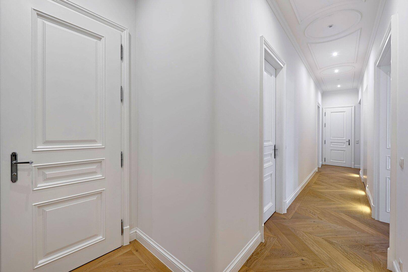 Langer Flur mit elegantem Fischgrätparkett, weißen Türen und dekorativer Decke.