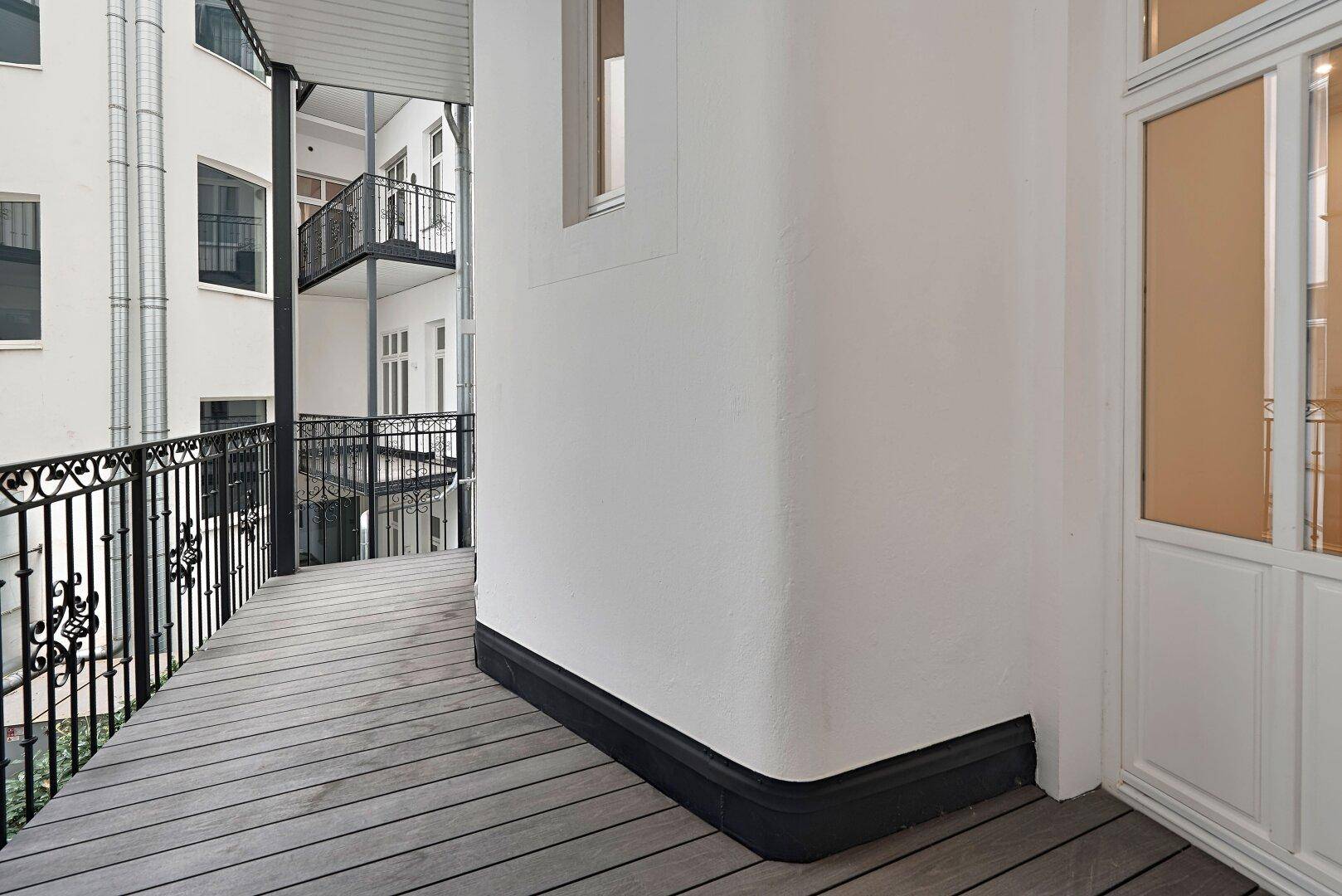 Geräumiger Balkon mit Holzdeck und schmiedeeisernem Geländer mit Blick auf den Innenhof.