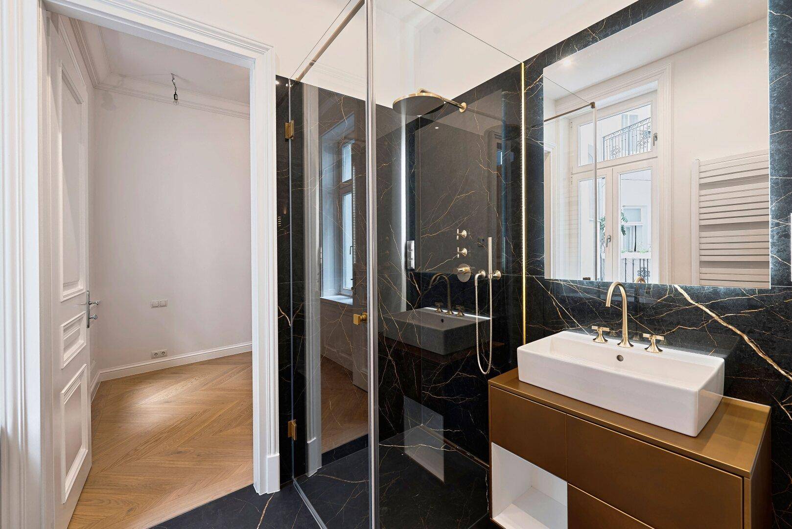 Modernes Badezimmer mit schwarzen Marmorfliesen, Glasdusche und eleganten Goldarmaturen.