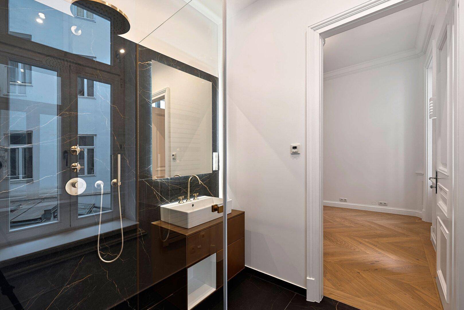 Elegantes Badezimmer mit schwarzem Marmor, moderner Dusche und stilvollem Waschtisch.
