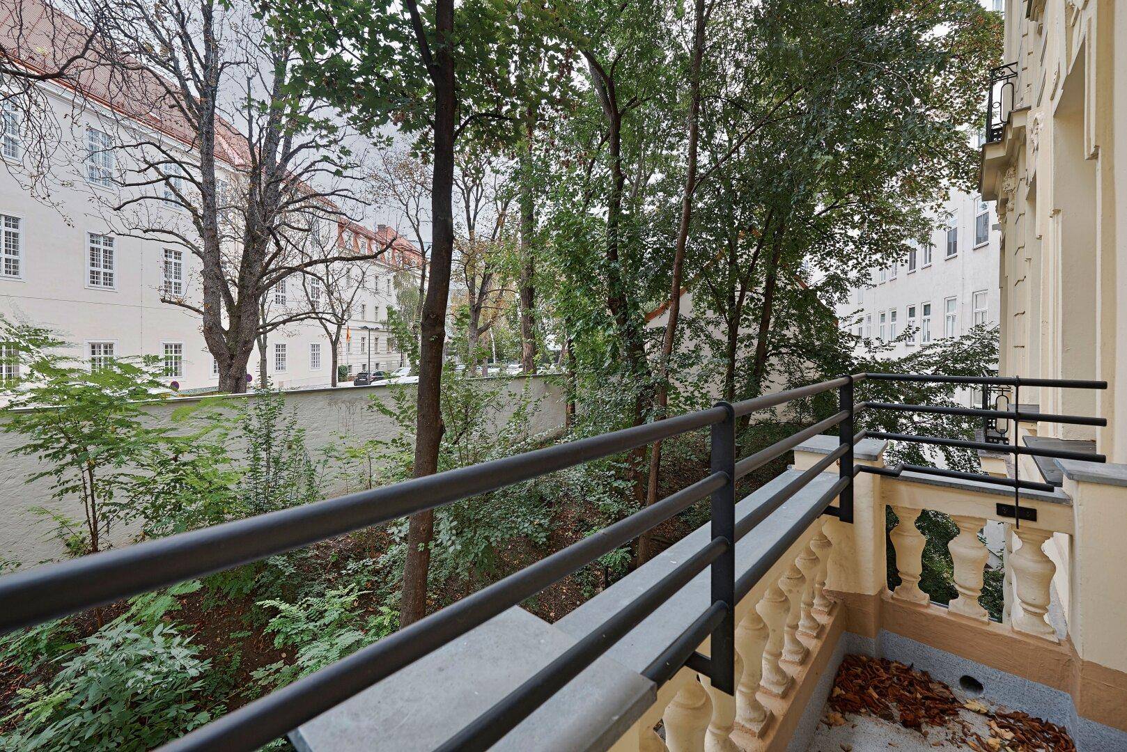 Balkon mit Blick auf einen grünen Innenhof und umliegende Gebäude.