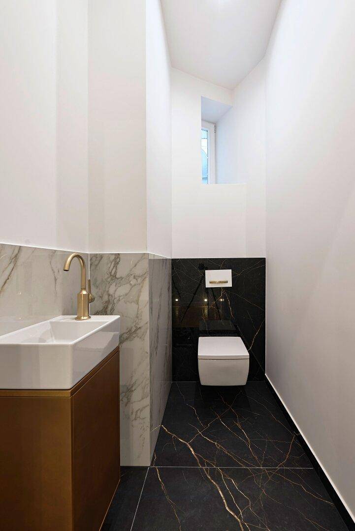 Schmales Gäste-WC mit Marmorfliesen, wandhängender Toilette und kleinem Fenster.