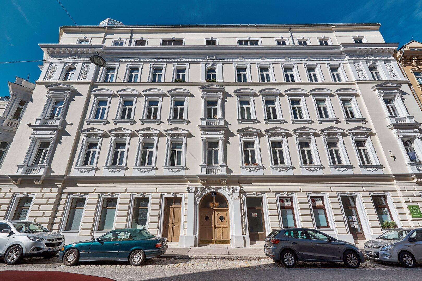 Historisches Gebäude mit reich verzierter Fassade und vielen Fenstern an einer Stadtstraße.
