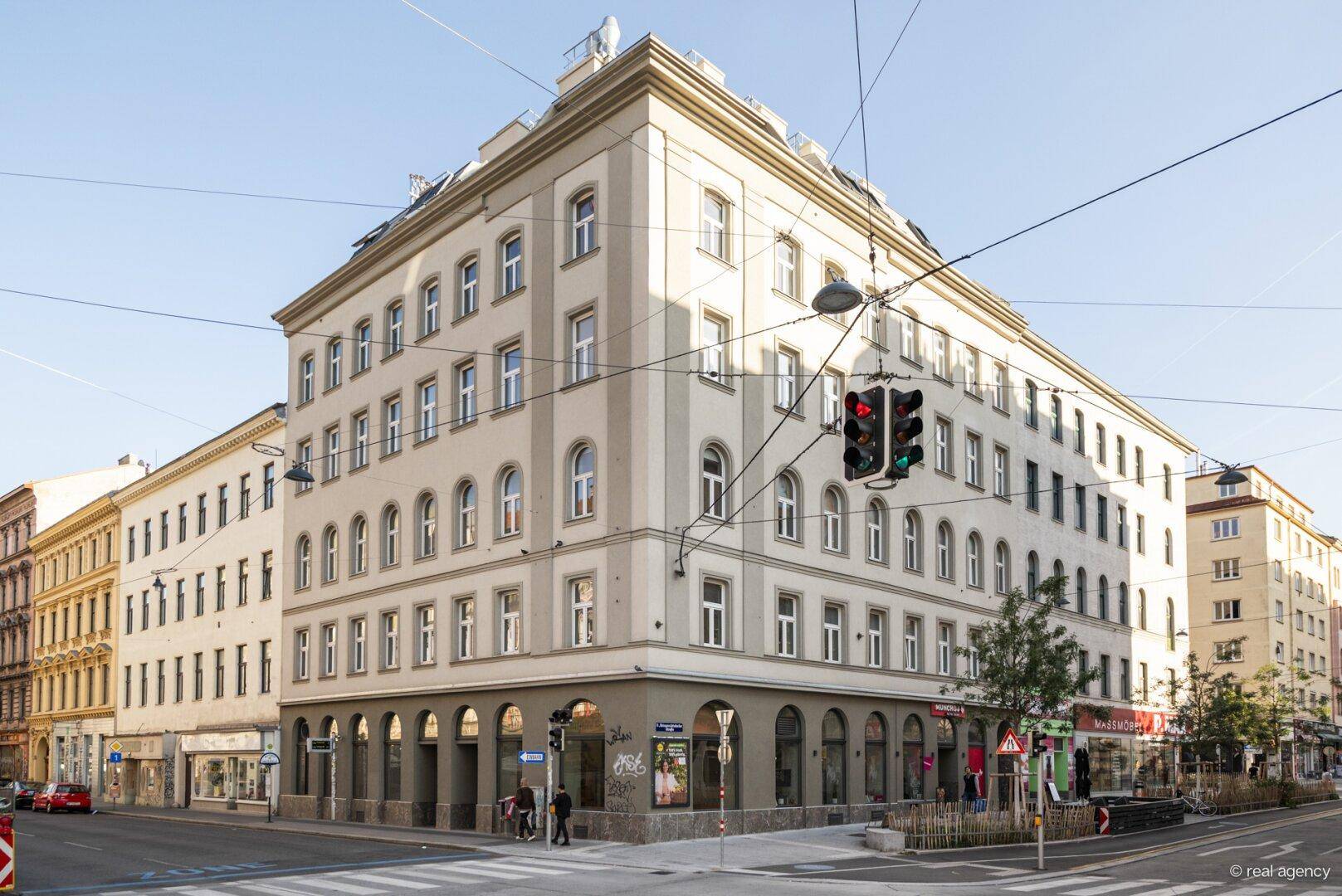 Historisches Eckgebäude in der Stadt mit vielen Fenstern und Geschäften im Erdgeschoss, das eine belebte Straße überblickt.