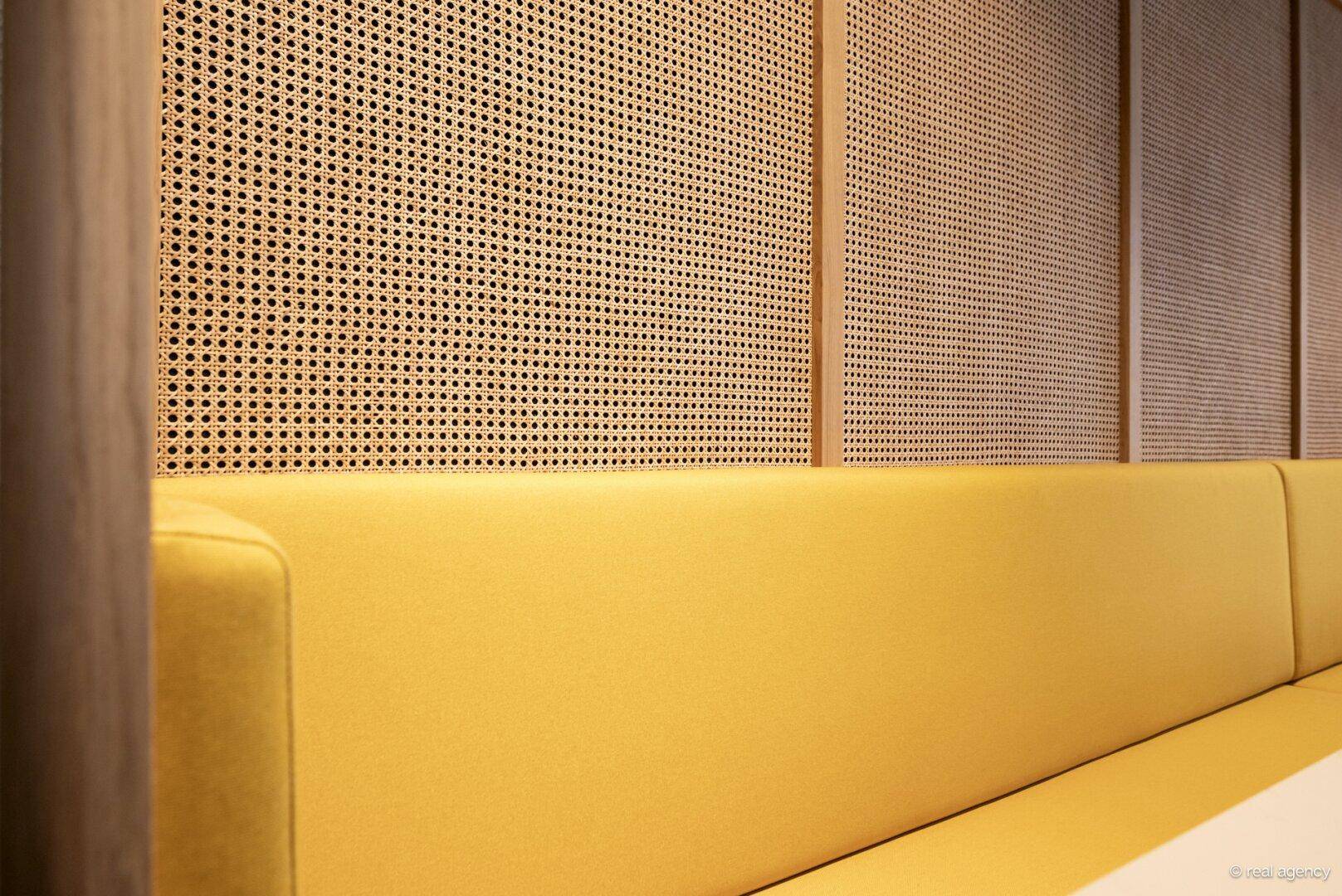 Detailansicht einer gelben Sitzbank mit Rattan-Verkleidung im Hintergrund, die eine warme und moderne Ästhetik bietet.