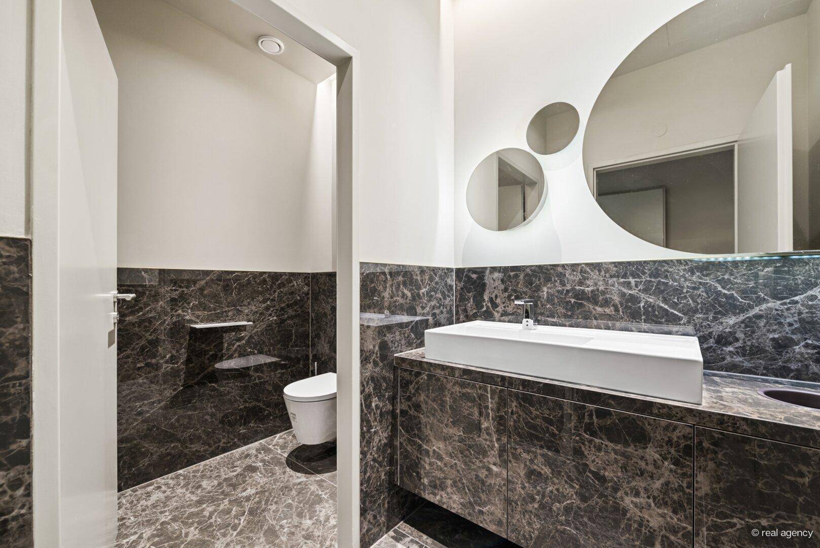 Modernes Gäste-WC mit dunklen Marmorfliesen, einem eleganten Waschbecken und einem wandmontierten WC.