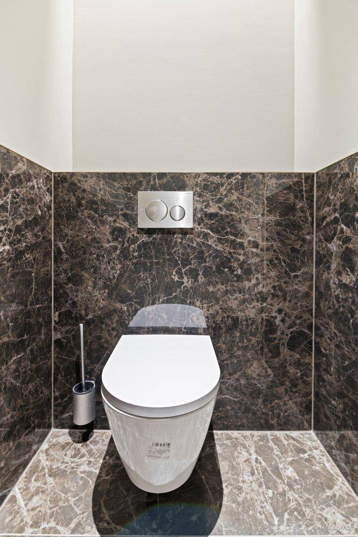 Wandmontiertes WC in einem modernen Gäste-WC mit dunklen Marmorfliesen und einer eleganten Spülplatte.