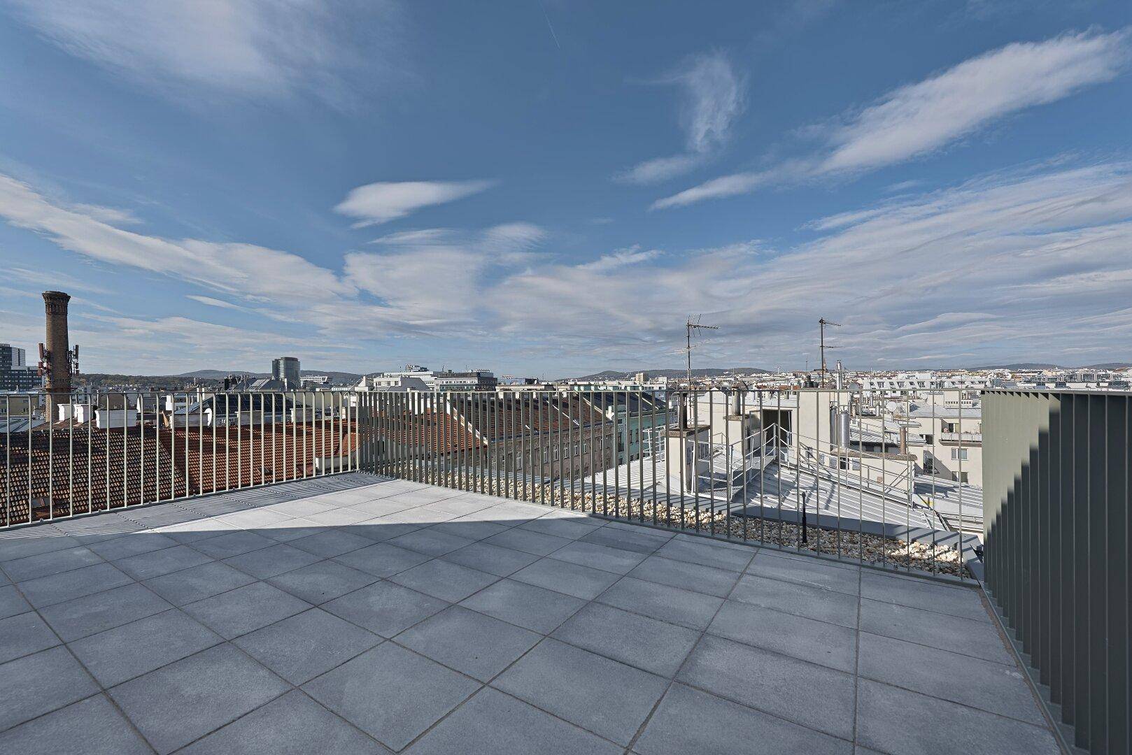 Weitläufige Dachterrasse mit Fliesenboden und modernem Geländer, bietet einen Panoramablick über die Stadt.