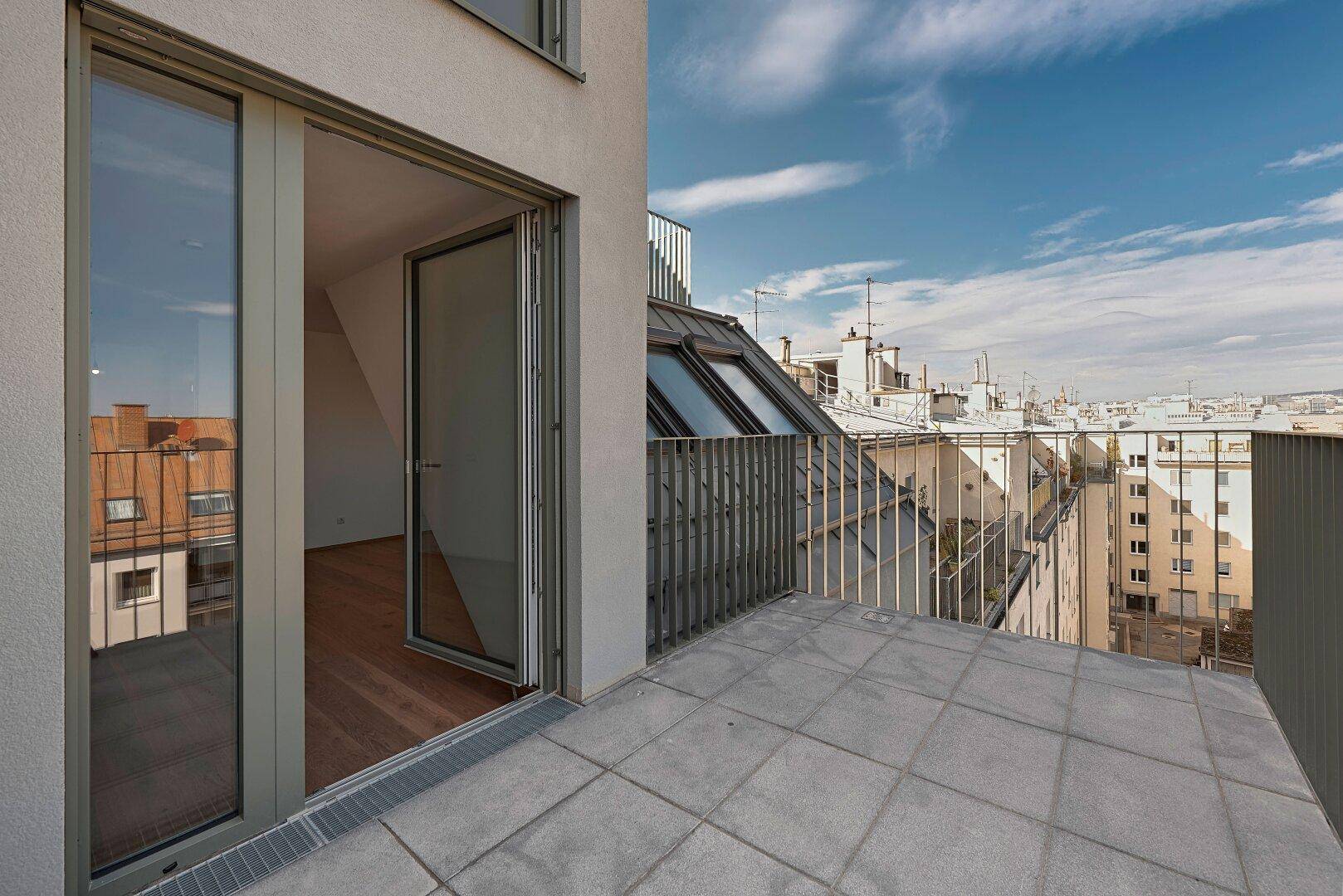 Dachterrasse mit Fliesenboden und offener Glastür, die den Zugang zu einem hellen Innenraum ermöglicht.