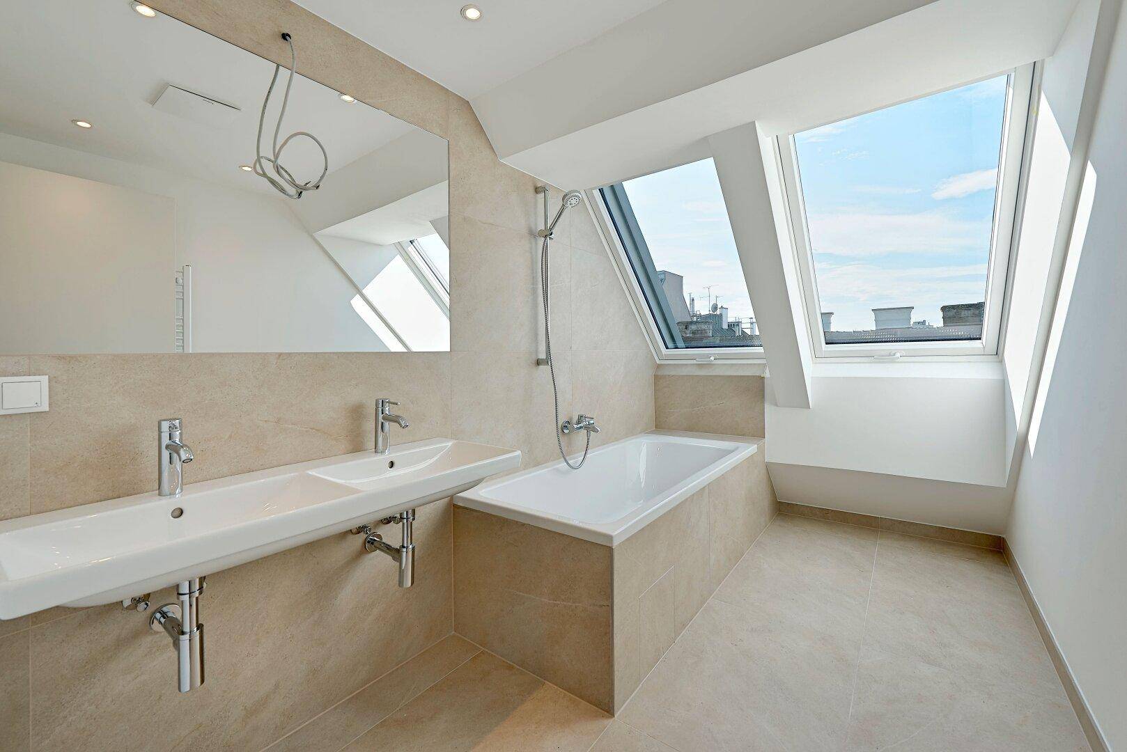 Modernes Badezimmer mit Doppelwaschbecken, Badewanne und zwei Dachfenstern für natürliches Licht.