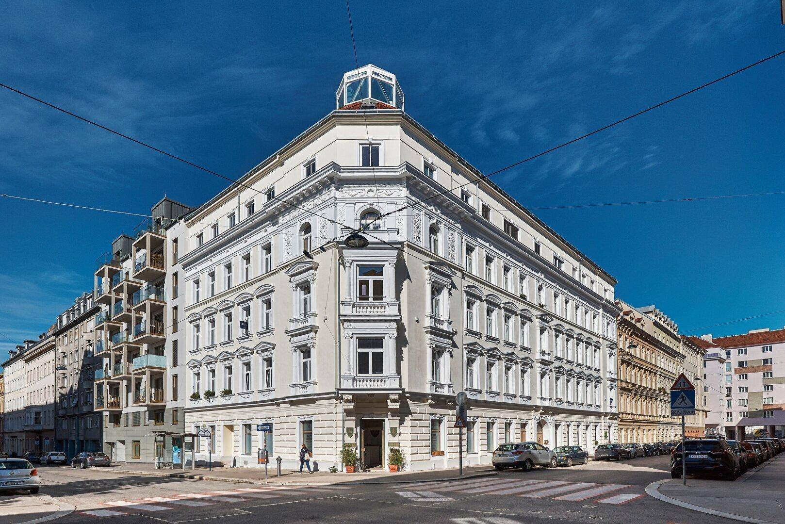 Historisches Eckgebäude mit klassischer Architektur und modernen Dachaufbauten in urbaner Umgebung.