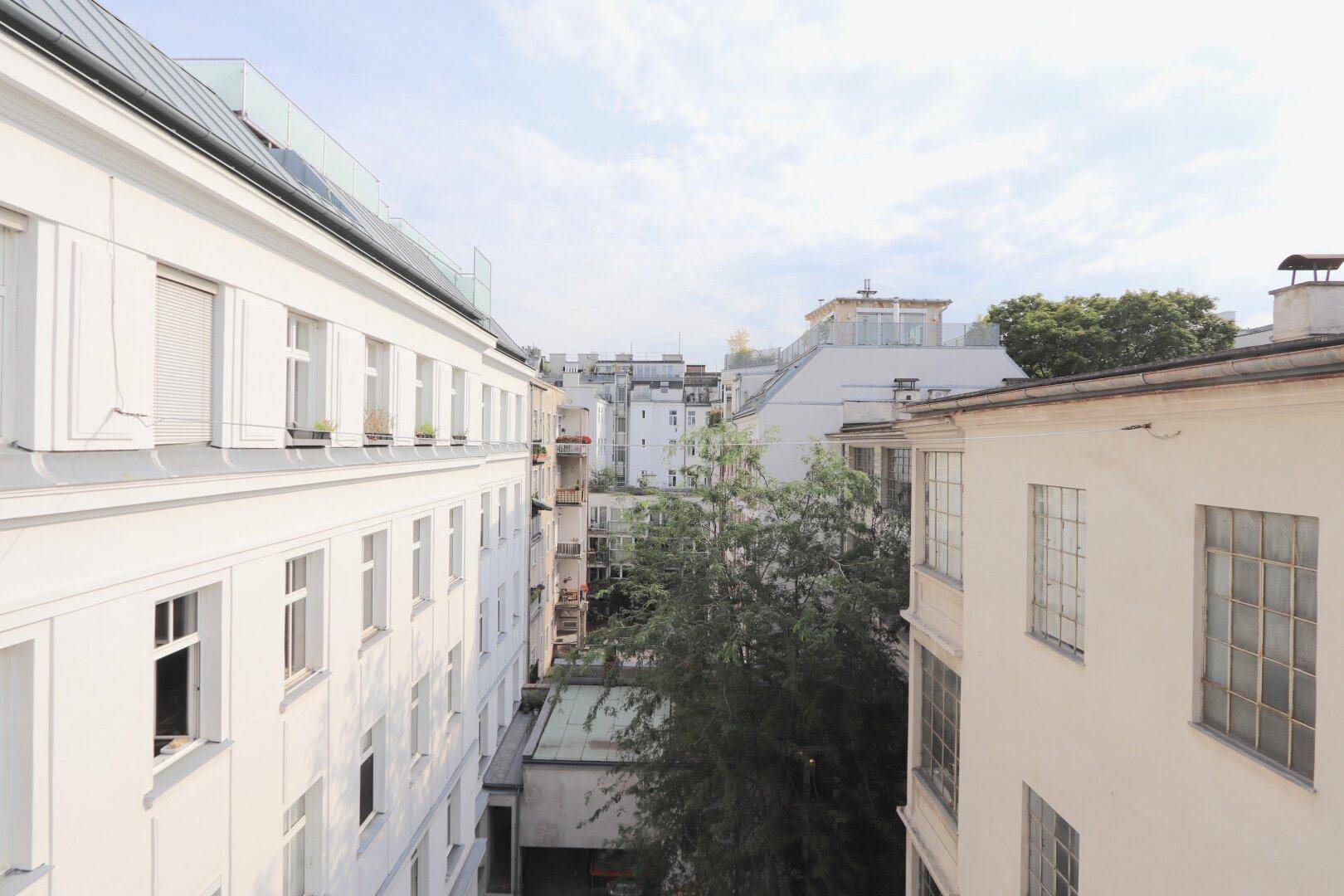 Blick auf die umliegenden Gebäude und einen Innenhof mit Bäumen unter einem bewölkten Himmel.