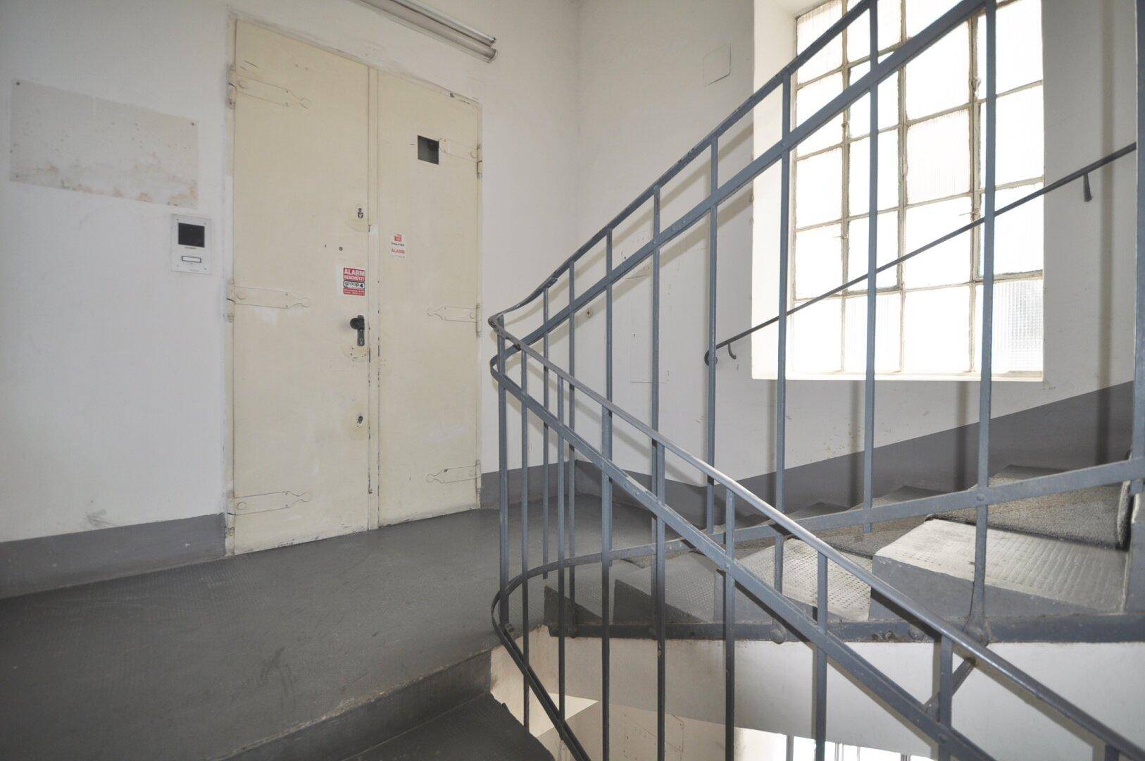 Treppenhaus mit Metallgeländer und großen Fenstern, das zu den oberen Etagen führt.