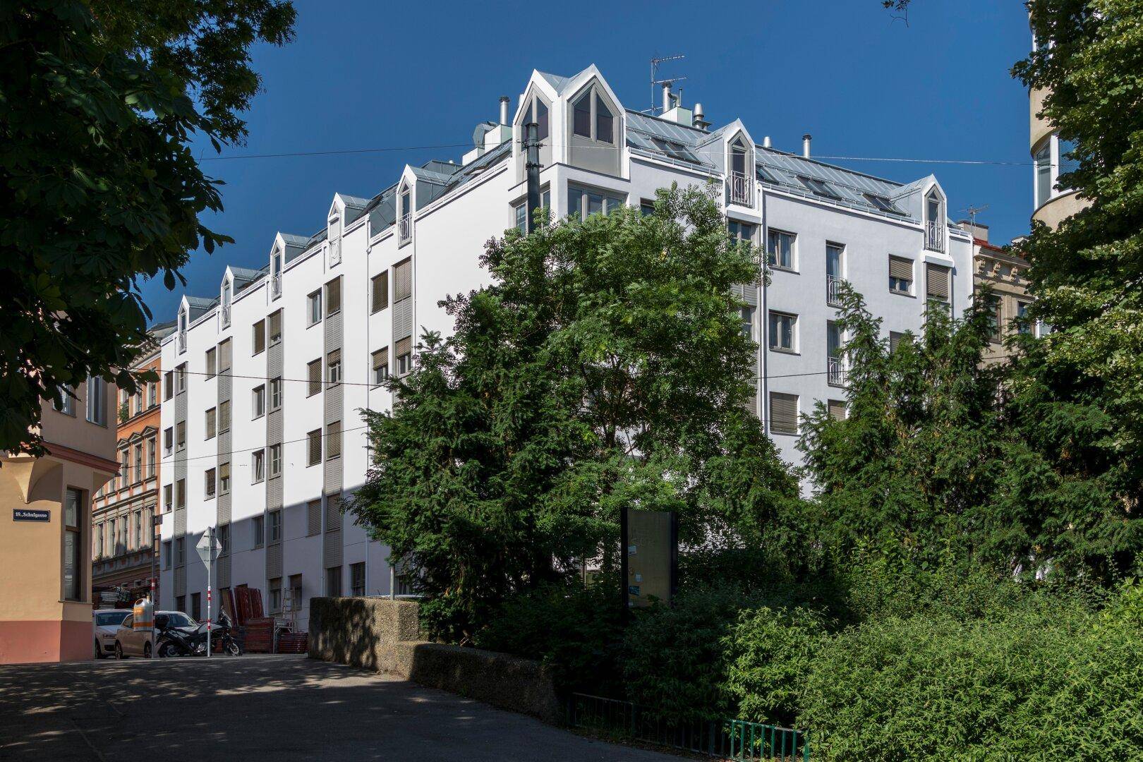 Ansicht des modernen Wohngebäudes mit weißer Fassade und vielen Fenstern, umgeben von üppigem Grün.