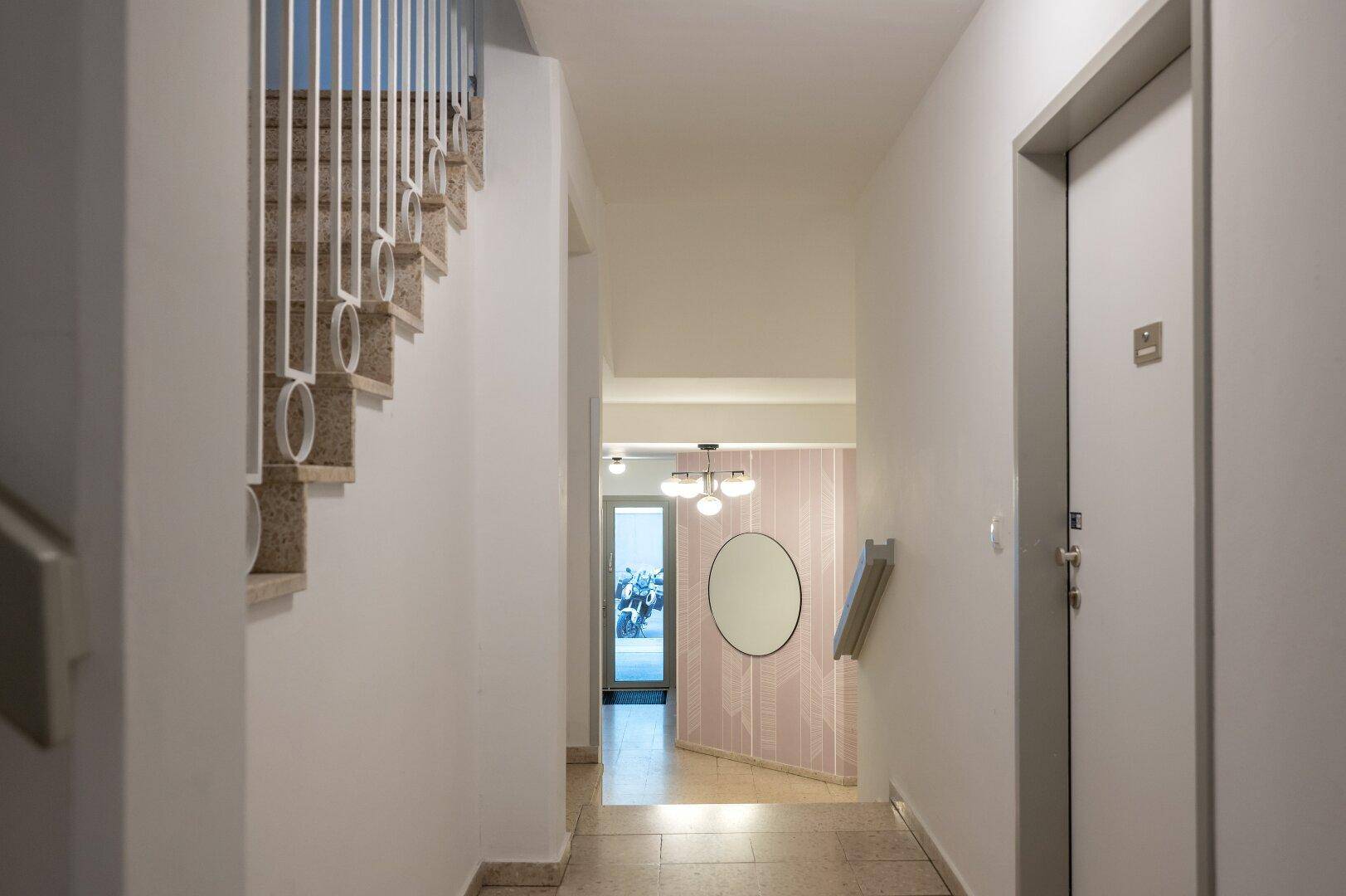 Eingangsbereich und Treppenhaus mit hellem Fliesenboden und modernem Spiegel an der Wand.