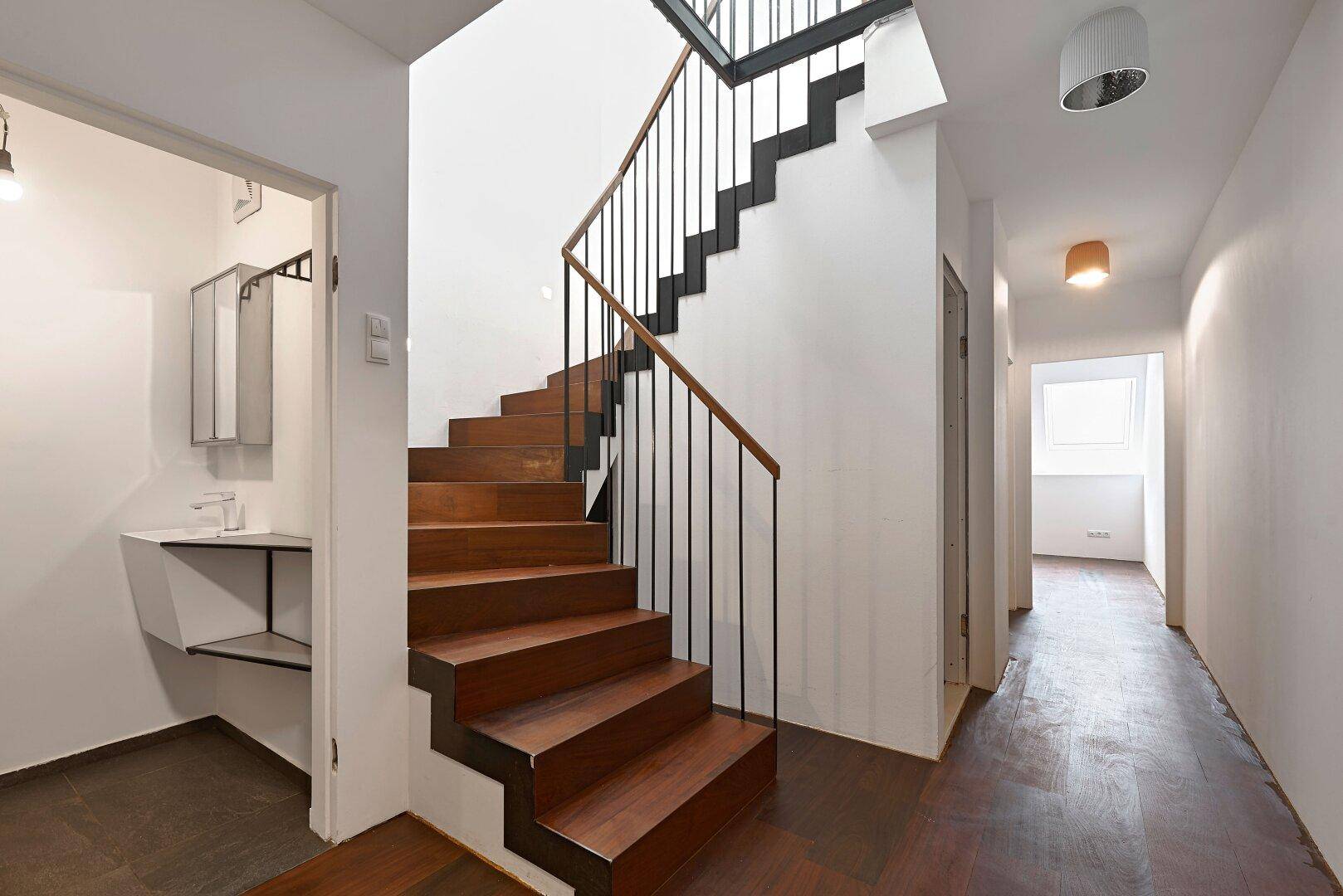 Heller Flur mit eleganter Holztreppe und Zugang zu einem kleinen Badezimmer.