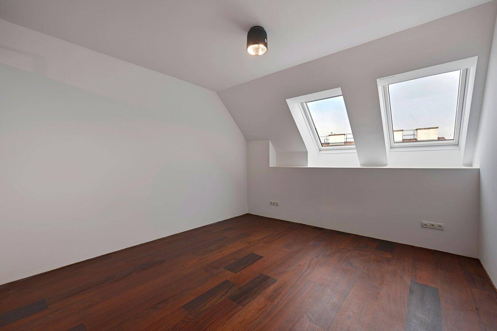 Helles Schlafzimmer mit dunklem Holzfußboden, Dachschrägen und zwei praktischen Dachfenstern.