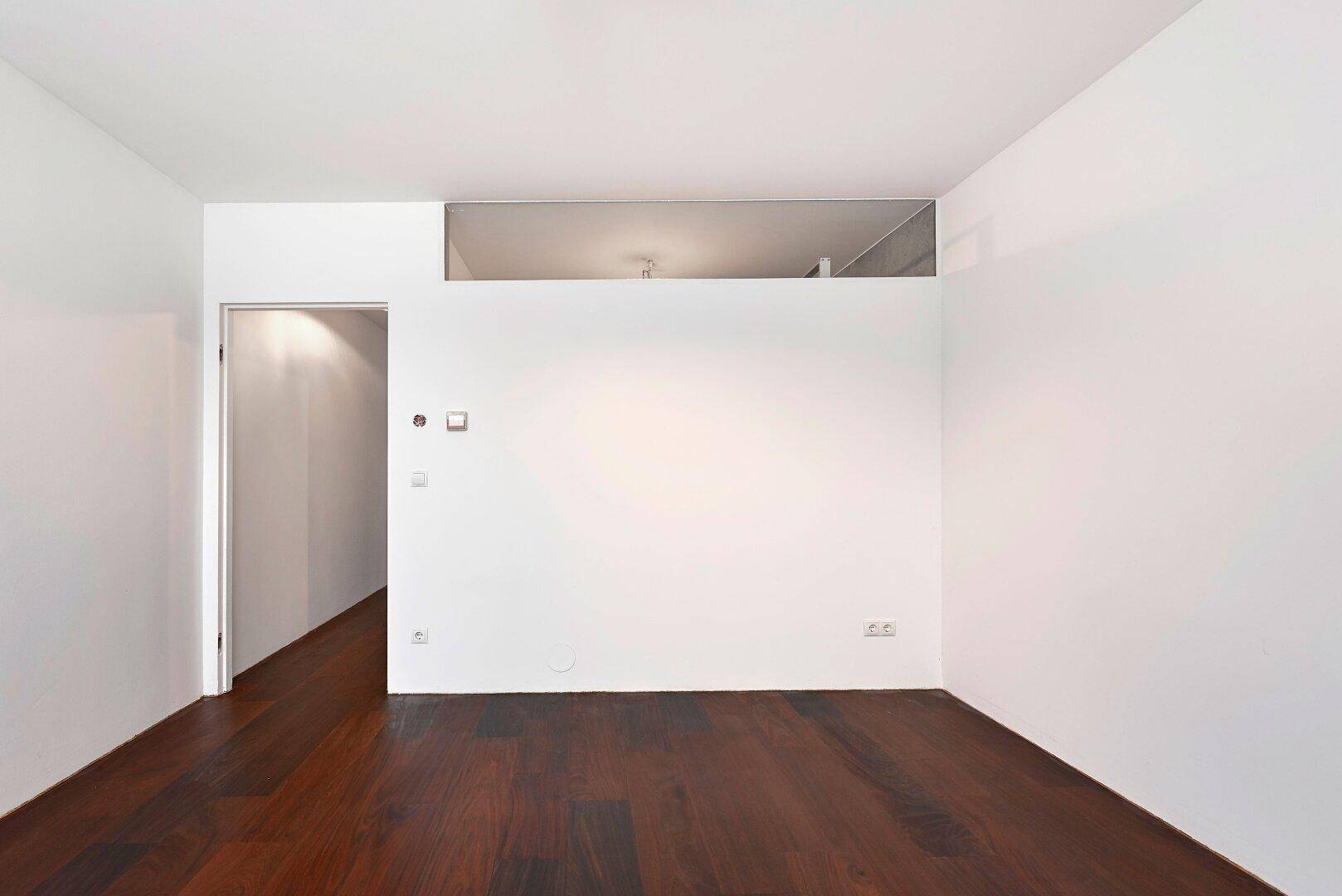 Schlichter Raum mit dunklem Holzfußboden und weißen Wänden, ideal für verschiedene Nutzungen.