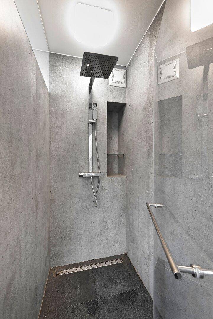 Moderne begehbare Dusche mit Regenduschkopf und grauen Fliesen an Wänden und Boden.
