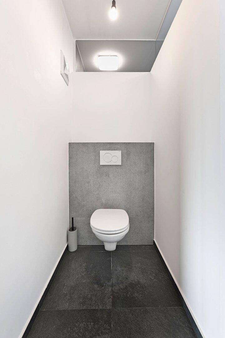 Modernes Gäste-WC mit wandhängender Toilette und dunklen Bodenfliesen in minimalistischem Design.