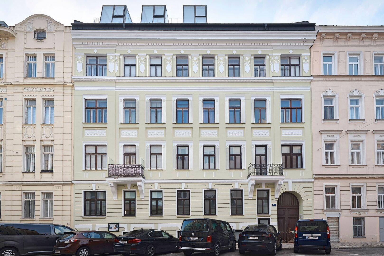 Historische Fassade eines Altbaus mit zahlreichen Fenstern und kleinen Balkonen an einer Stadtstraße.