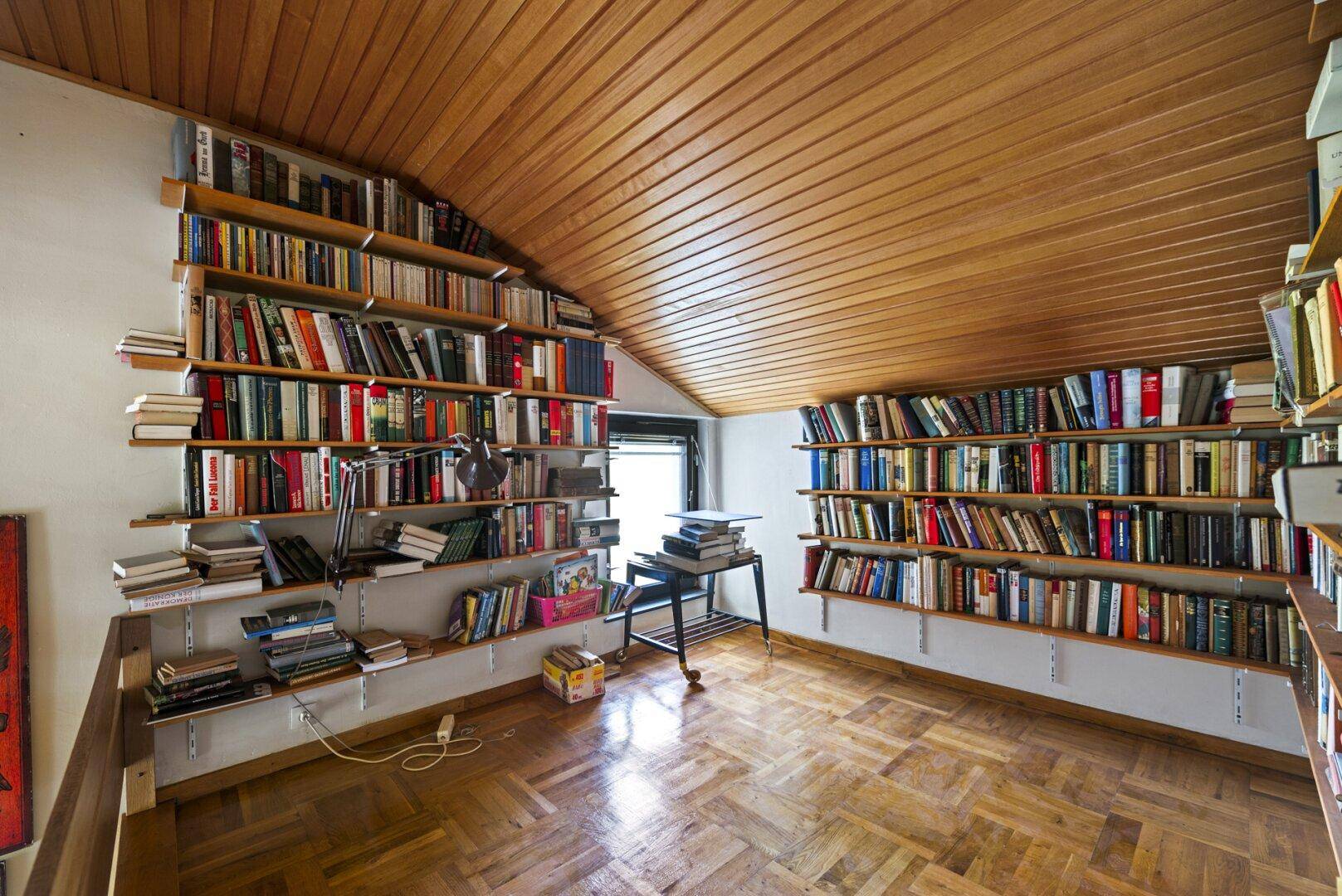 Gemütliches Lesezimmer mit raumhohen Bücherregalen und warmer Holzvertäfelung an der Decke.