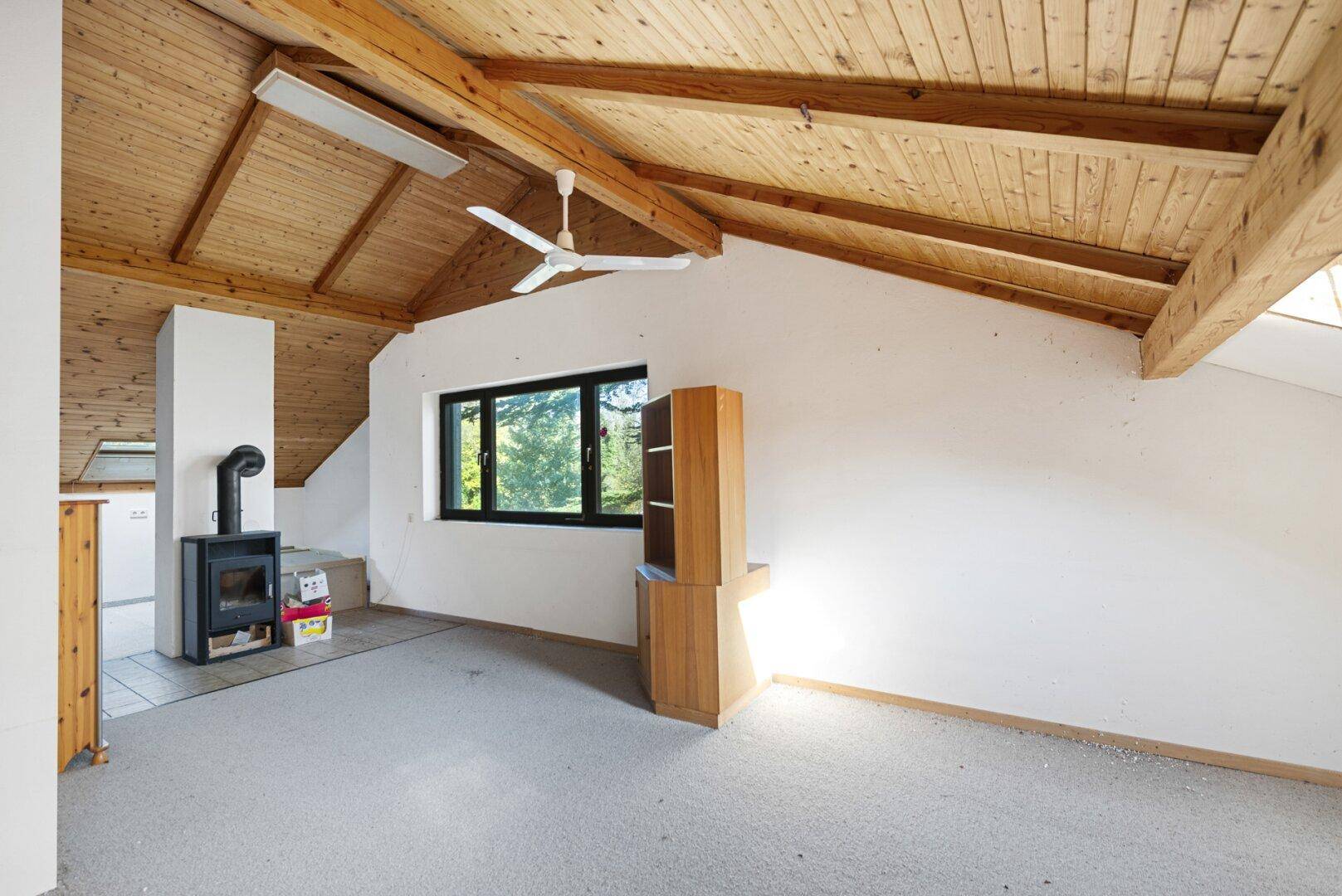 Heller Raum mit Holzdachschräge, sichtbaren Balken und einem modernen Holzofen.