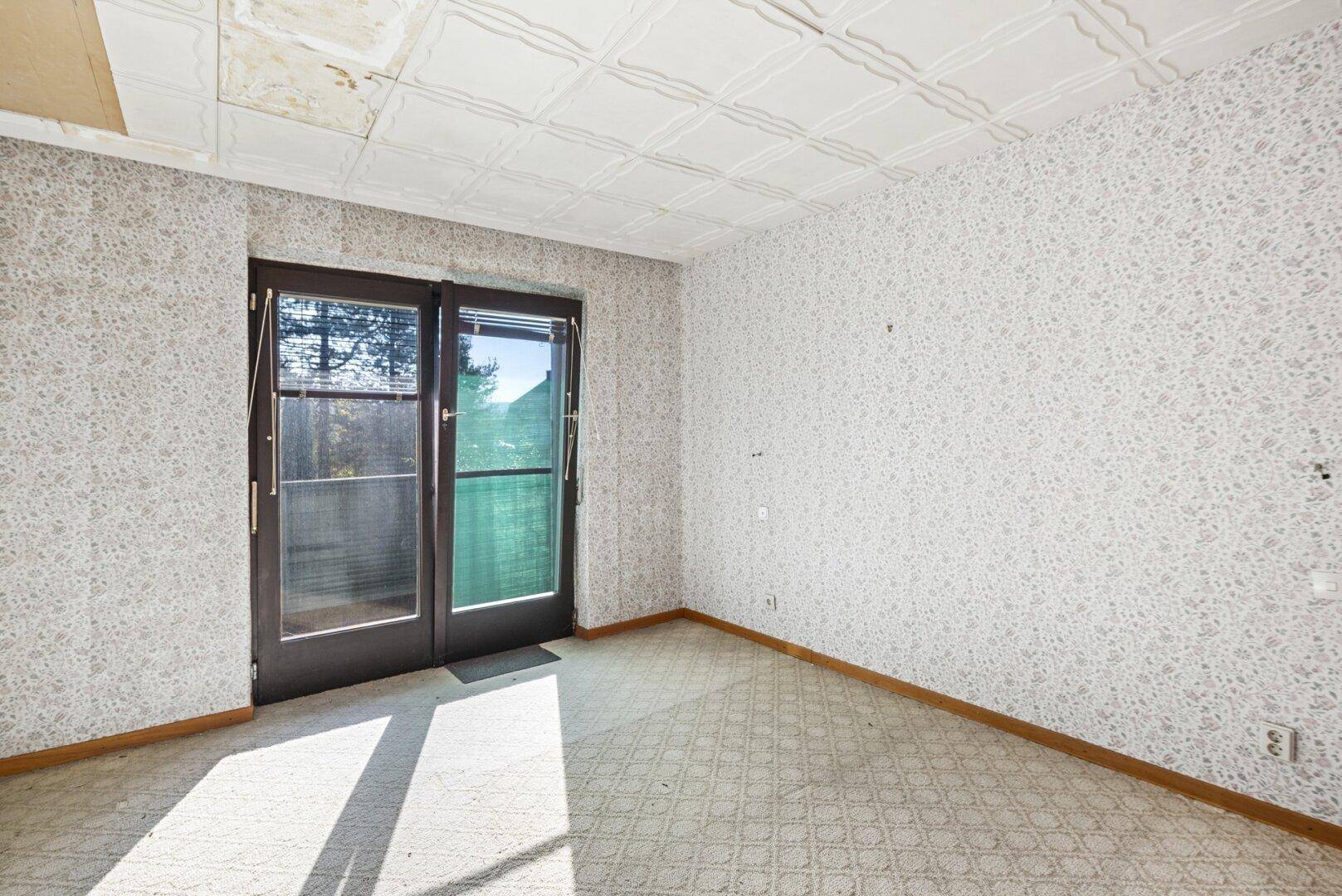 Zimmer mit gemusterter Tapete, Kassettendecke und Zugang zu einem Außenbereich.