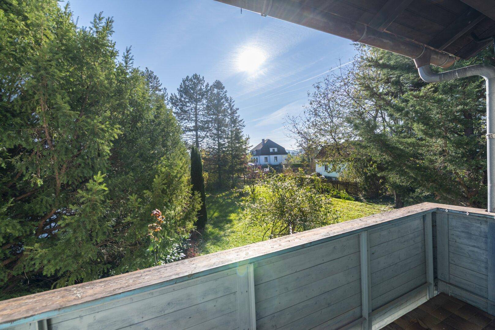 Sonniger Balkon mit Blick auf den grünen Garten und die umliegende Landschaft.
