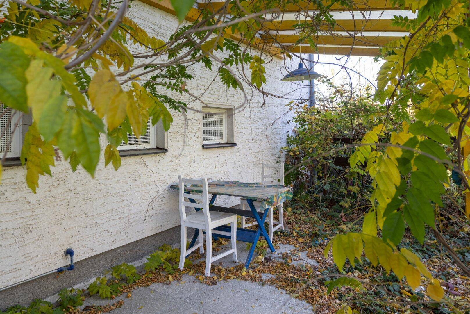 Gemütlicher Außenbereich mit Sitzgelegenheiten unter einer Pergola, umgeben von Herbstlaub.