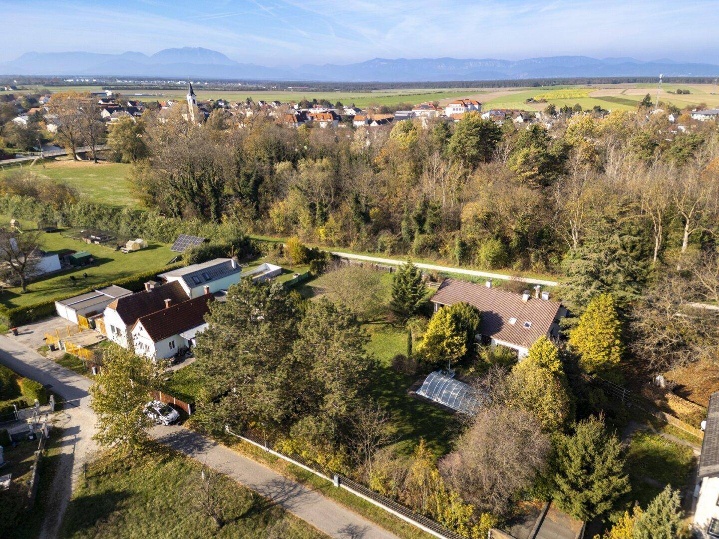 Weitläufige Luftaufnahme einer ländlichen Siedlung mit Feldern und Bergen im Hintergrund.