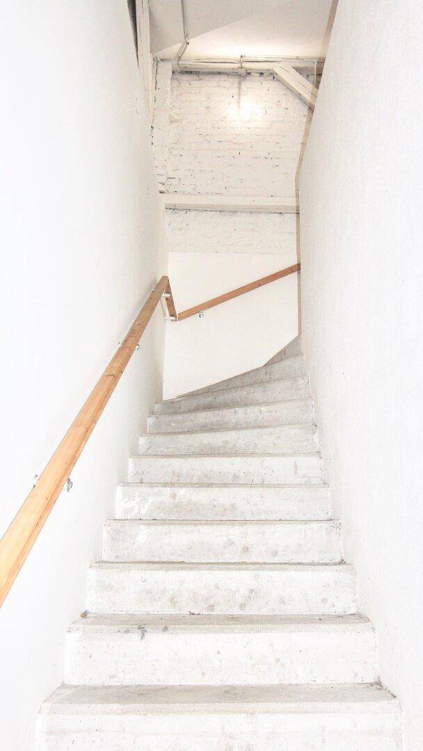 Heller Treppenaufgang mit Holzgeländer und weißen Wänden, der in ein oberes Stockwerk führt.