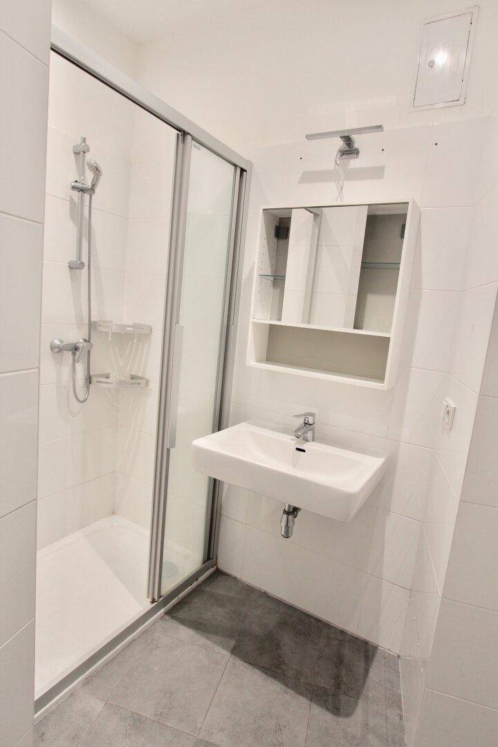 Modernes Badezimmer mit weißer Duschkabine, Waschbecken und Spiegelschrank.