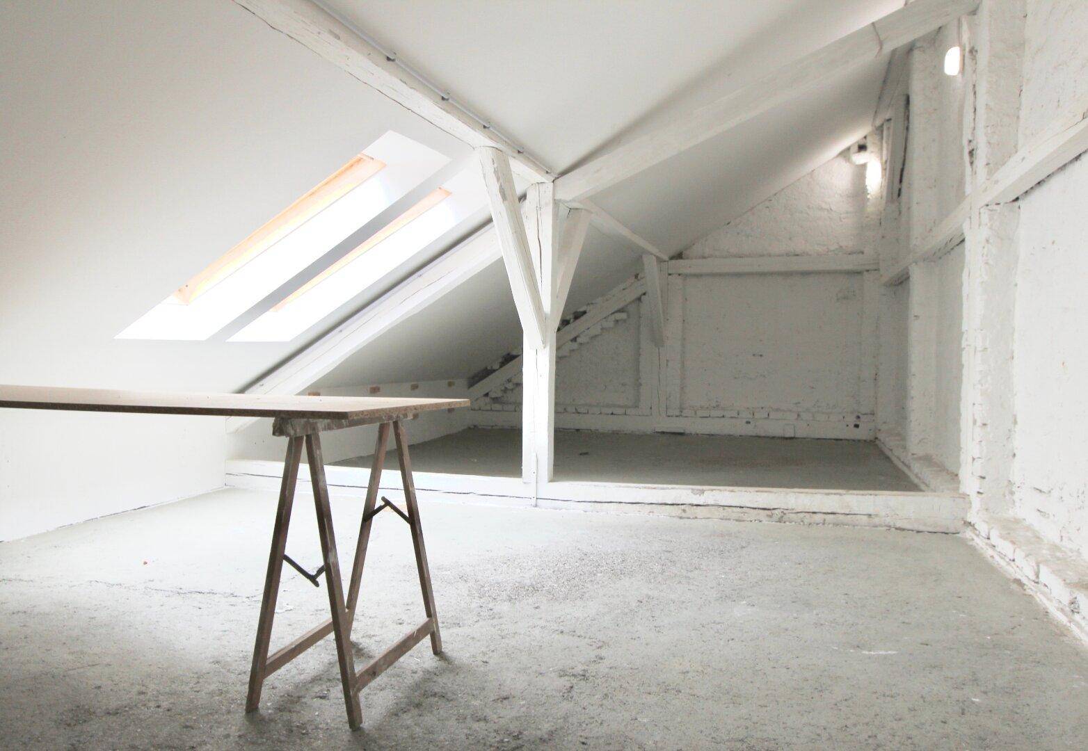Heller Dachbodenraum mit sichtbaren Holzbalken, Dachfenstern und schrägen Wänden.
