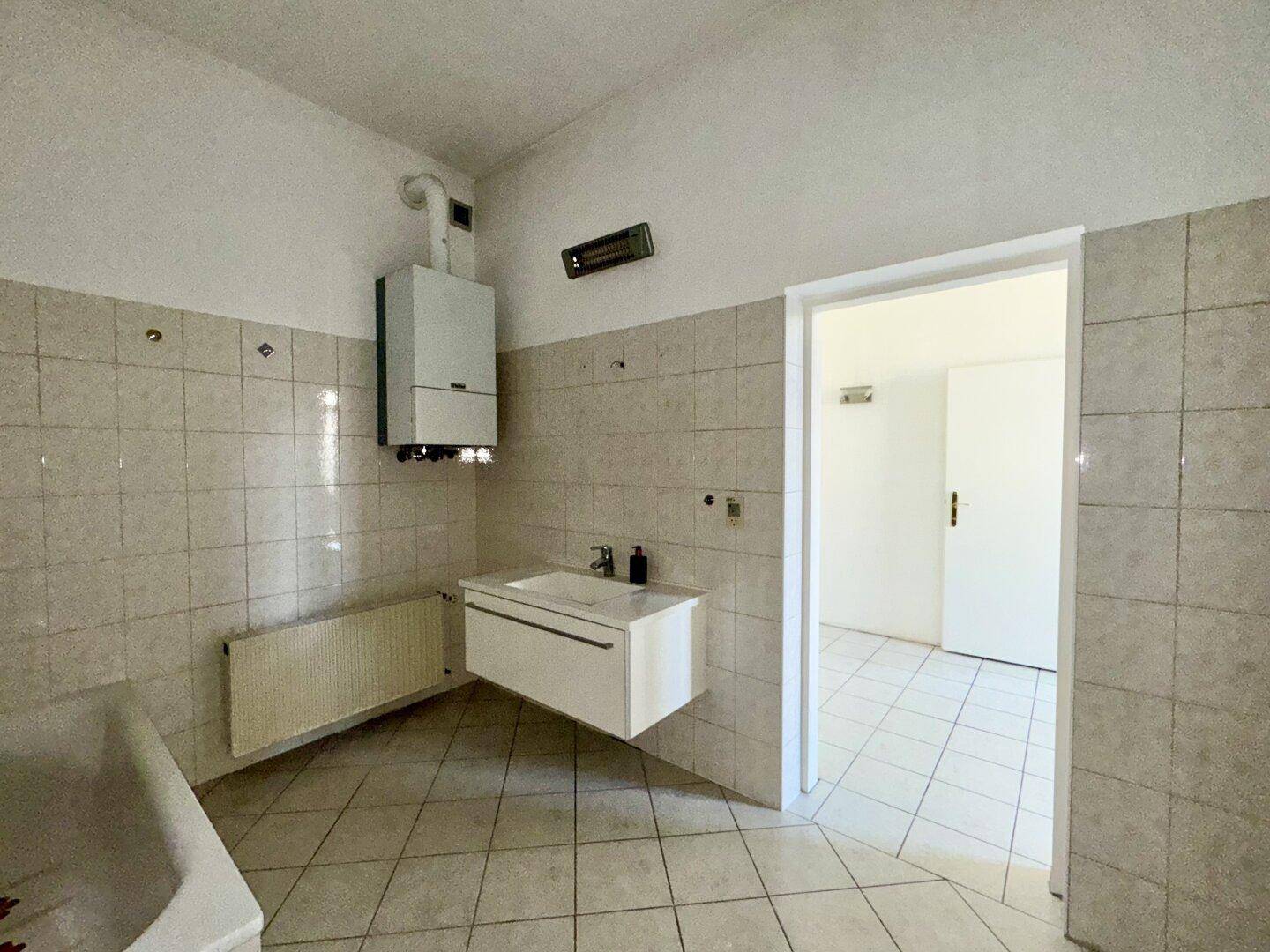 Badezimmer mit Badewanne, Waschbecken und Wandfliesen, inklusive Heizung und Warmwasserbereiter.