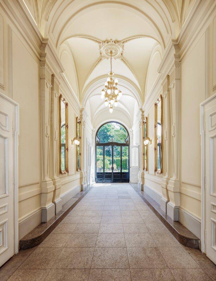 Eleganter Flur mit hohen Gewölbedecken, Stuckverzierungen und großem Bogenfenster zum Garten.
