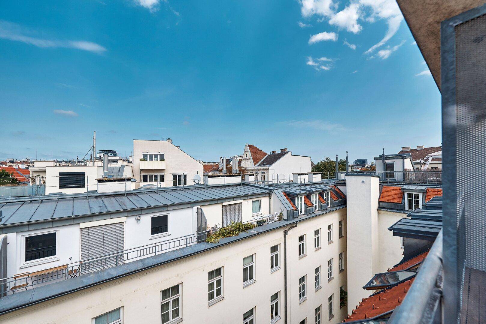 Weitläufiger Blick über die Dächer der Stadt mit verschiedenen Gebäuden und einem blauen Himmel.