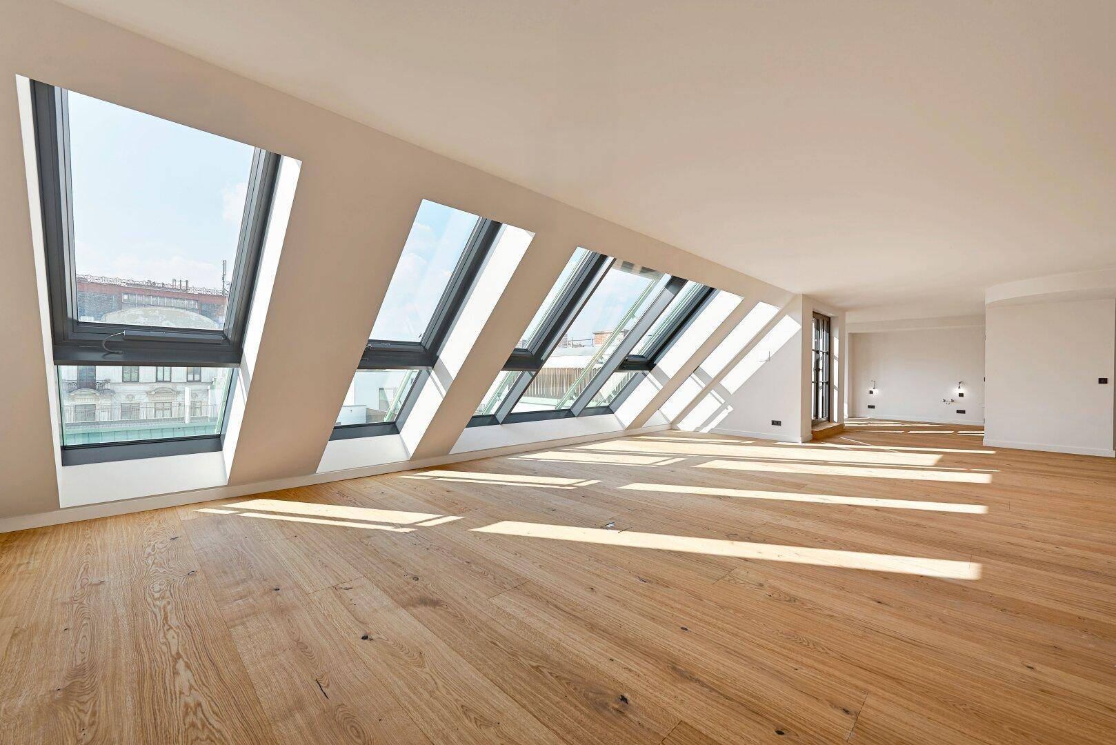 Geräumiges Dachgeschosszimmer mit mehreren schrägen Dachfenstern, die viel Tageslicht hereinlassen.