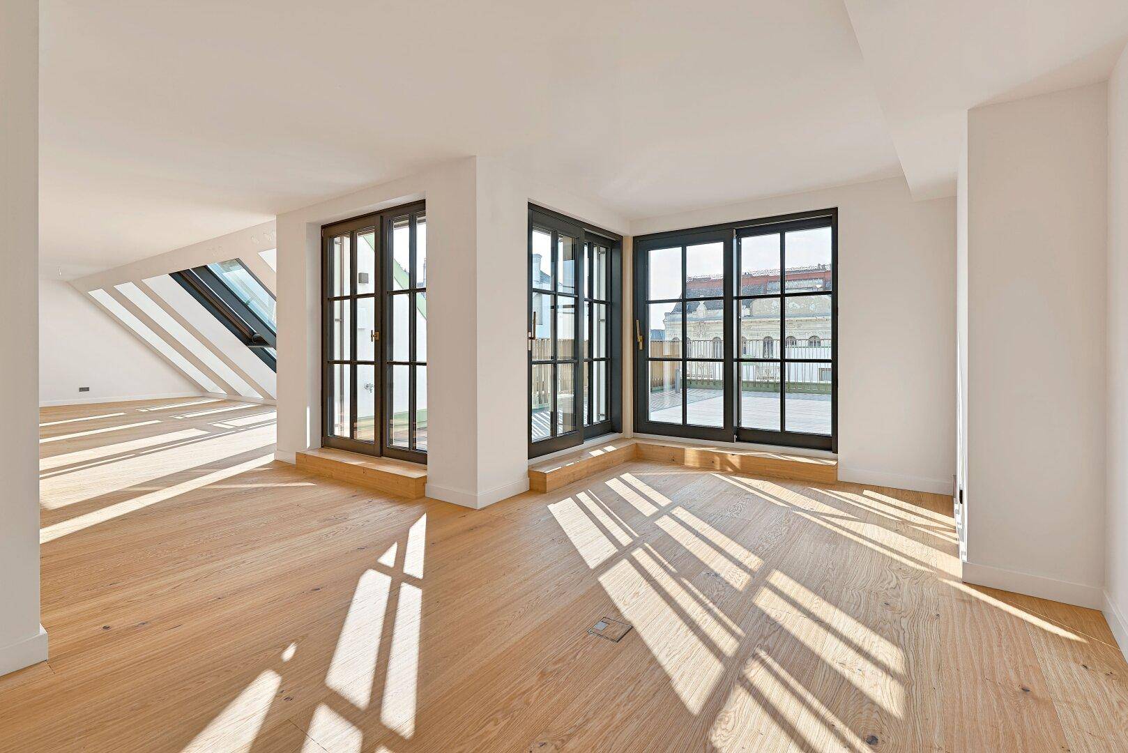 Heller Raum mit Holzboden und großen Fenstertüren, die Zugang zu einem Außenbereich bieten.