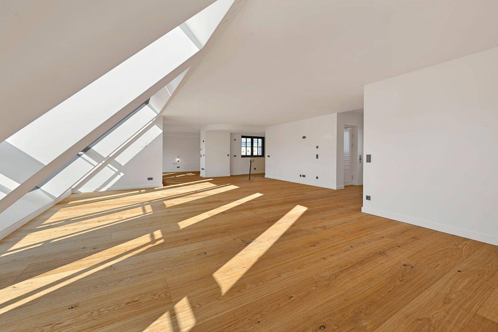Weitläufiger, lichtdurchfluteter Raum im Dachgeschoss mit schrägen Fenstern und hellem Holzboden.