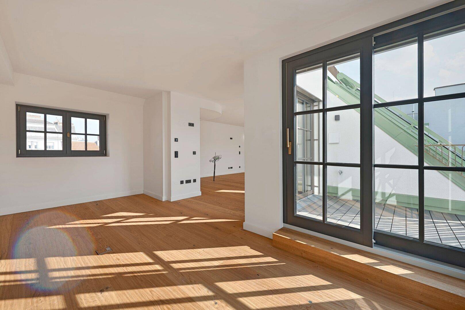 Lichtdurchfluteter Raum mit Holzboden und Zugang zu einem Außenbereich, ergänzt durch ein kleines Fenster.
