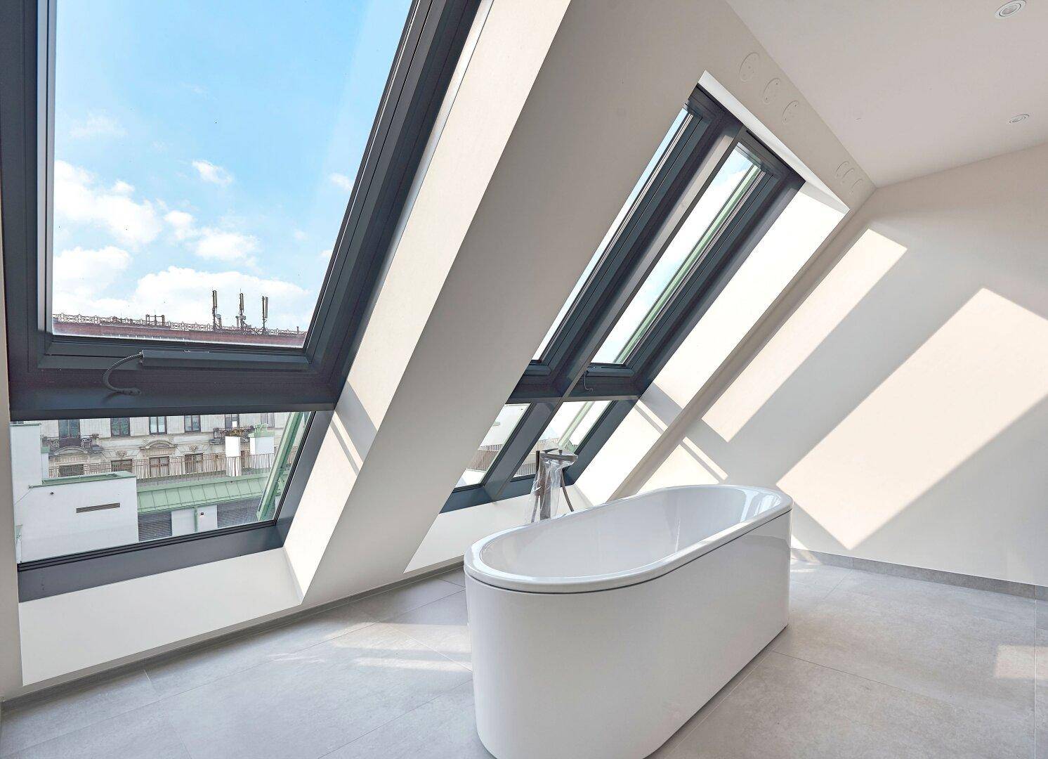 Modernes Badezimmer mit freistehender Badewanne unter großen Dachfenstern und Fliesenboden.
