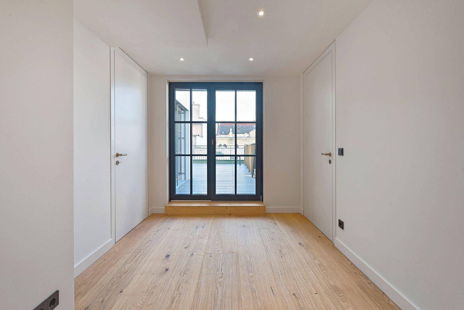 Helles Schlafzimmer mit Holzboden und Fenstertüren, die auf eine Terrasse führen.