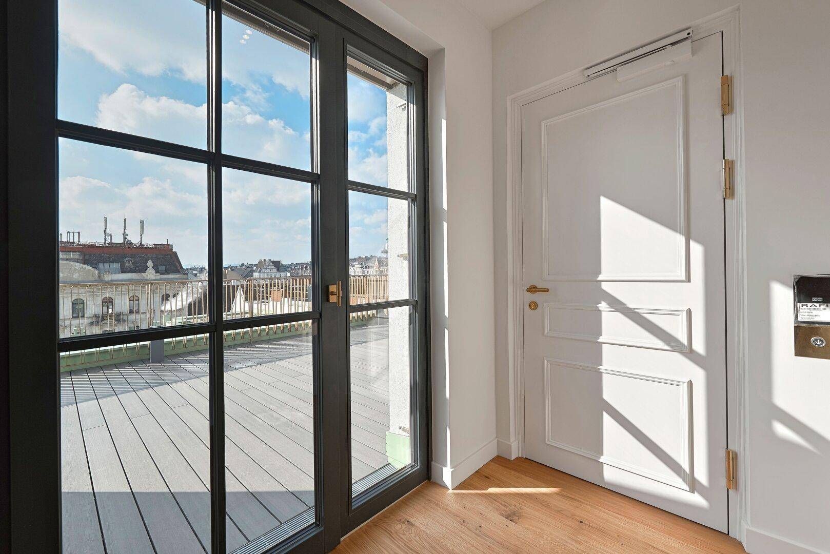 Heller Bereich mit Holzboden und einer eleganten Tür, die zu einer sonnigen Dachterrasse führt.