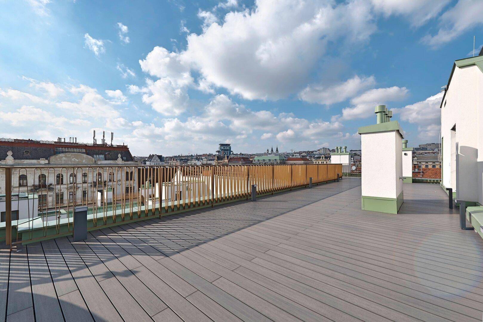 Weitläufige Dachterrasse mit Holzdielen und Blick über die Stadt, ideal zum Entspannen.