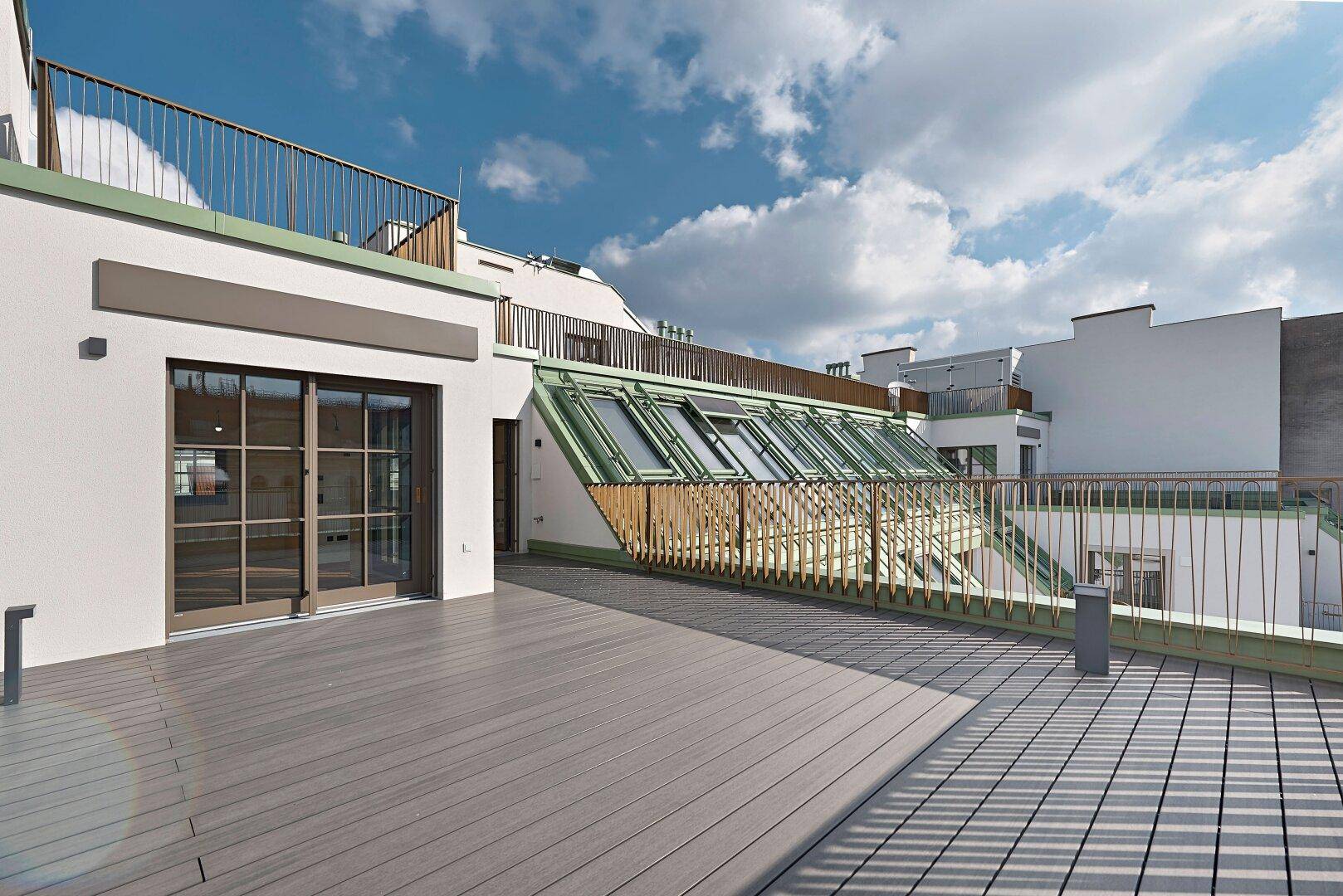 Große Dachterrasse mit Holzdielen und Zugang zu den Innenräumen, umgeben von Stadtblick.