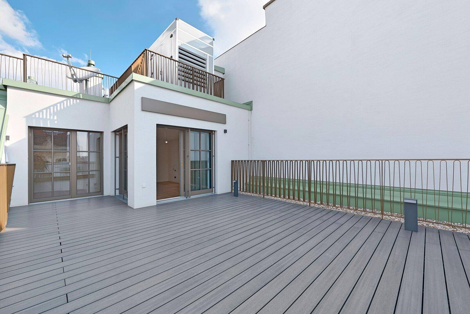 Weitläufige Dachterrasse mit Holzdielen und Blick auf die umliegenden Gebäude und den Himmel.