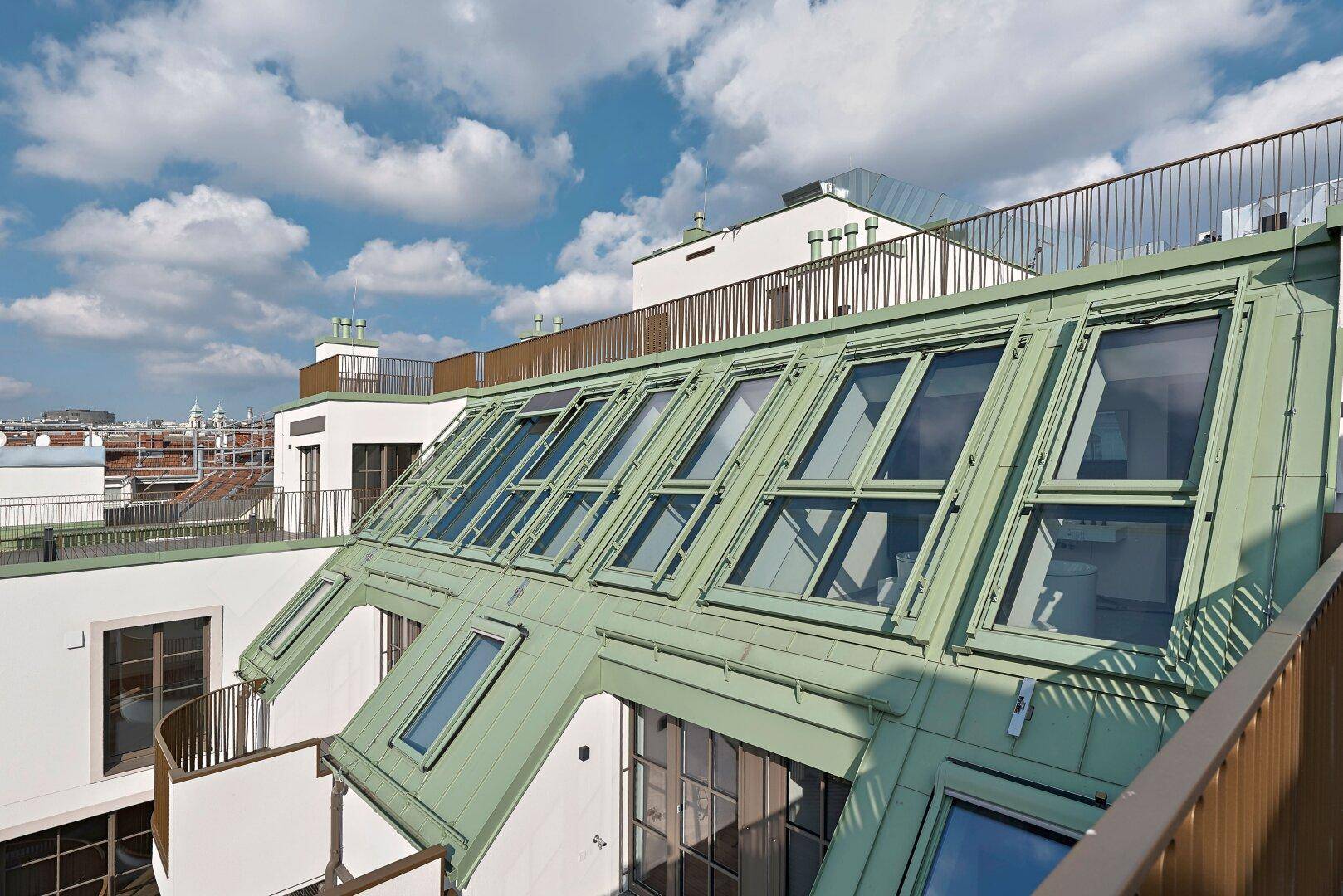 Dachterrasse mit Blick auf die Stadt und die grüne Dachkonstruktion, umgeben von einem Geländer.