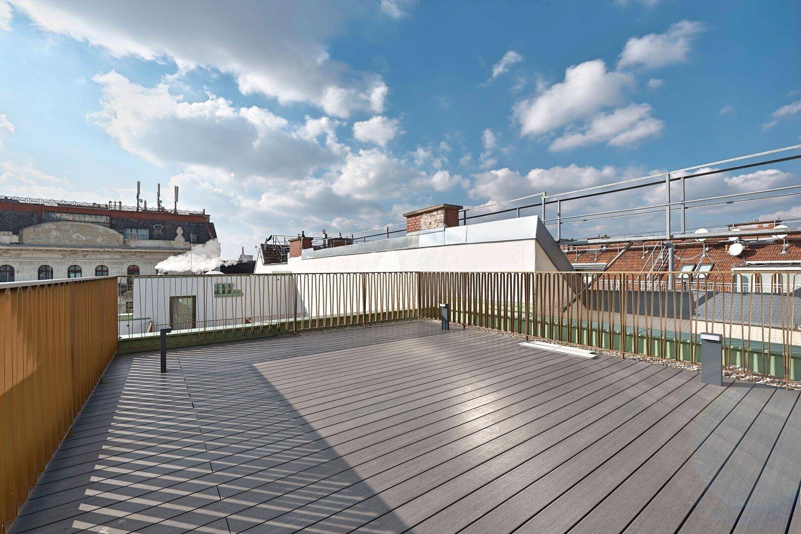 Große Dachterrasse mit Holzdielen und weitem Blick über die Dächer der Stadt.