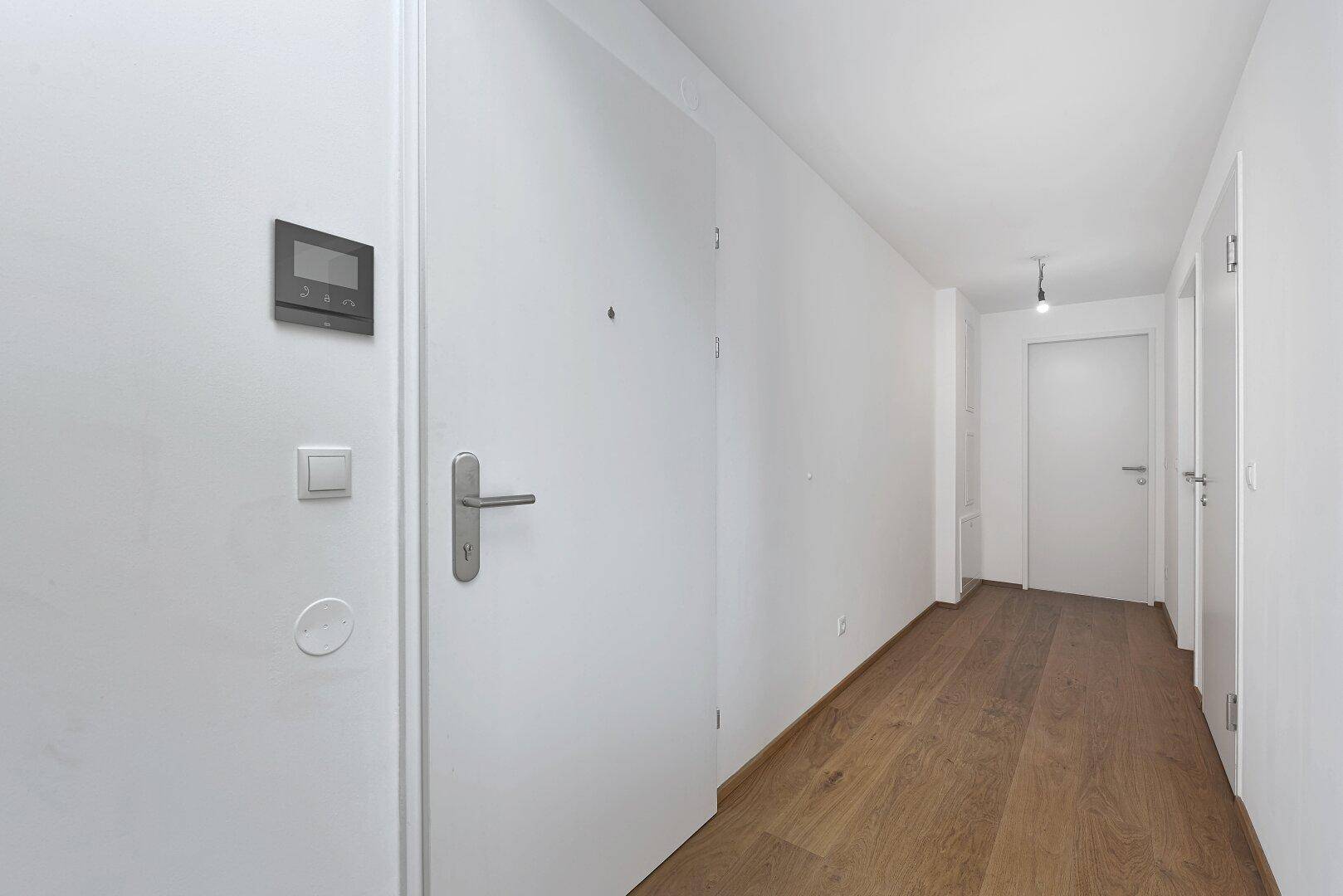 Heller Flur mit Holzboden und modernen weißen Türen, ausgestattet mit einer Gegensprechanlage.